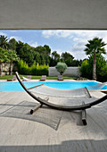 Hammock on curved stand in front of modern pool below palm trees
