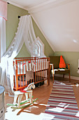 Cot with canopy in vintage-style nursery with green walls