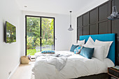 Bed against black panelled wall in front of floor-to-ceiling window with garden view