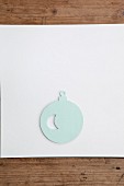 Christmas-tree bauble cut out of pale blue paper on white surface