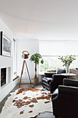Black leather armchair, studio lamp and cowhide rug in front of fireplace