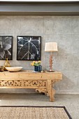 Table lamp an vase of flowers on carved wooden console table against concrete wall