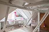 Desk below window in attic room with white roof beams