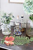Sycamore and fern leaves amongst flowers and bottles of spirits on table