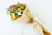 Bouquet of colourful freesias being wrapped in brown paper