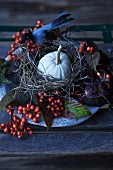 Herbstliche Tischdeko mit Kürbis im Vogelnest, roten Beerenzweigen und Blättern