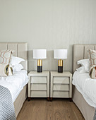 Lamps on two shiny bedside cabinets between twin beds