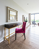 Hot-pink upholstered chair at console table with gilt frame below mirror