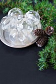 Glass Christmas-tree baubles on silver platter next to conifer branches and pine cones