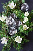 Glass Christmas-tree baubles, green conifer branches and hellebore flowers
