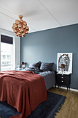 Red bedspread on bed against blue-grey wall