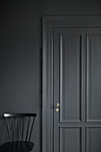 Black chair against grey wall with grey panelled door