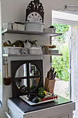Crockery on shelves, mirror, knife block and vegetables on chopping board in rustic kitchen