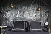 Double bed against black relief wall with gilt bedside lamps