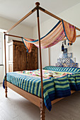 Striped blanket on four-poster bed with tiles on wall at head end