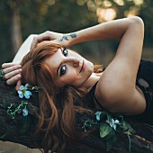 Red-haired woman with tattoo lying on tree branch