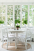 Cushions with ruffles on white chairs at round table in Scandinavian conservatory