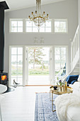 Chandelier and log-burner in high-ceilinged, white living room with terrace doors