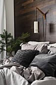 Pendelleuchte an einem Wandgestell über dem Bett mit grauer Wäsche