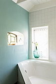 Small window in pale turquoise wall in bathroom with corner bathtub
