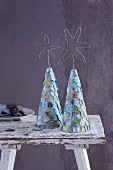 Stylised, conical Christmas trees covered in overlapping pieces of maps and decorated with messages of love and peace