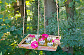 DIY-Vogelbad mit Schwimmkerzen und Malven- und Hortensienblüten an langen Seilen hängend