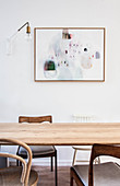 Various wooden chairs around simple dining table below artwork on wall