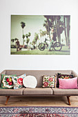 Scatter cushions on retro sofa below large photo on living room wall