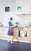 Woman in bright kitchen with wooden cabinets and dark floor