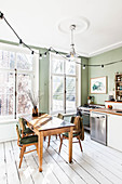 Green wall, white wooden floor and dining set in front of large windows in kitchen-dining room