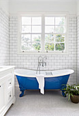 Freestanding blue bathtub in narrow white bathroom