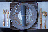 Gold cutlery and round plate on square charger plate in shades of grey