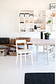 Wooden table and chair in front of suitcases and baskets on bench and white shelves