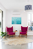 Two purple wing chairs and a cowhide rug against a water image