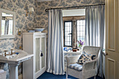 Pedestal sink, wicker armchair and toile de jouy wallpaper in blue and white bathroom