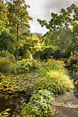 Garden pond surrounded by perennials and grasses in autumn garden (Les Jardin de Castillon, France)