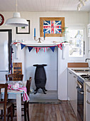 Country house kitchen with iron stove in disused fireplace, above it DIY pennant chain and England flag in picture frame