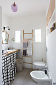 Eclectic bathroom with curtain below washstand, towel rail, toilet and bidet