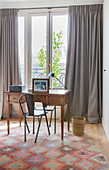 Metal chair at antique desk on colourful rug in front of window