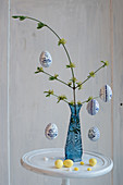 Easter eggs hung from branch in blue glass vase
