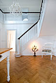 Stuhl und Kerzenleuchter in Halle mit Fischgrätparkett, Treppenaufgang und weißen Wänden