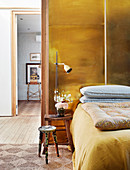 Gold wall behind bed with two stools used as bedside tables