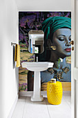 Mural wallpaper, wall-mounted mirror, pedestal sink and yellow side table in bathroom