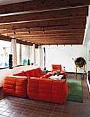 Orangefarbenes Designersofa im Wohnzimmer mit Balkendecke