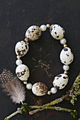 Circlet of threaded quail eggs and beads on black surface