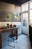Crockery and houseplants on old wooden table in kitchen with dark wall