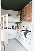 White, L-shaped fitted kitchen with one exposed brick wall