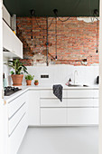 White, L-shaped fitted kitchen with one exposed brick wall