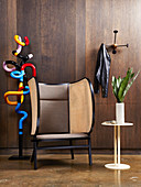 Colourful metal sculpture, designer wing-back chair and side table in front of wall with dark wooden panelling
