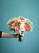 Hand hält Blumenstrauss aus Rosen, Pfingstrosen, Fresien und Kamillenblüten